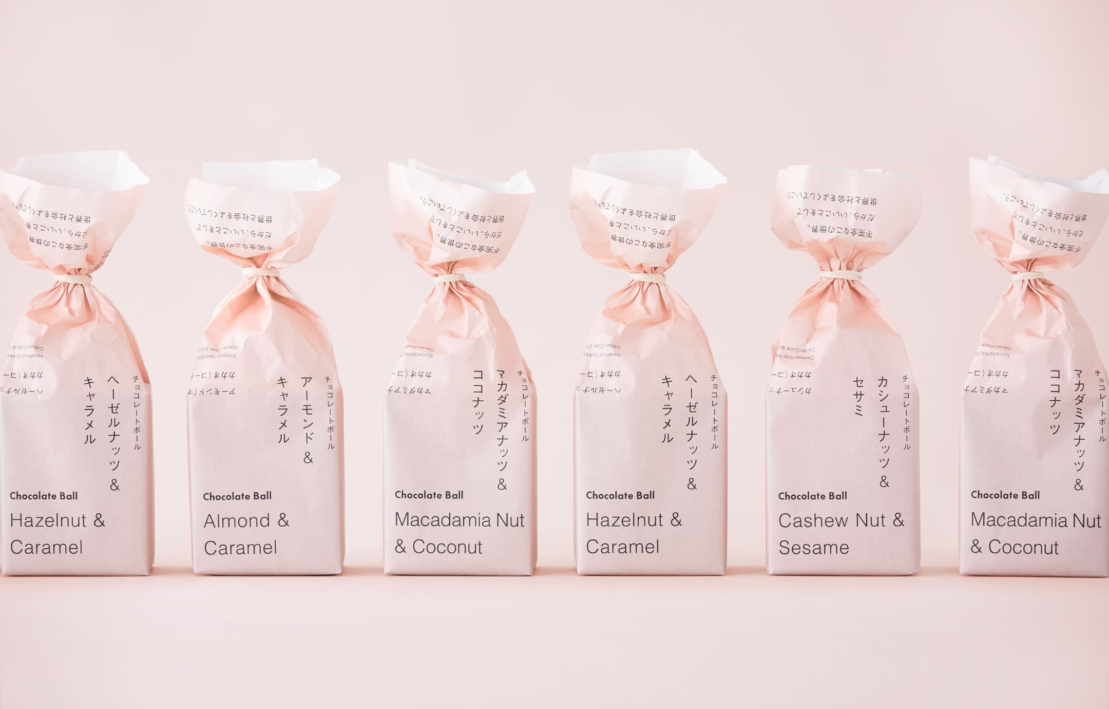 View of chocolate-ball packaging designed by 6D for Imperfect, a café in Tokyo. Image features six packages in pink wrapping paper with black type.