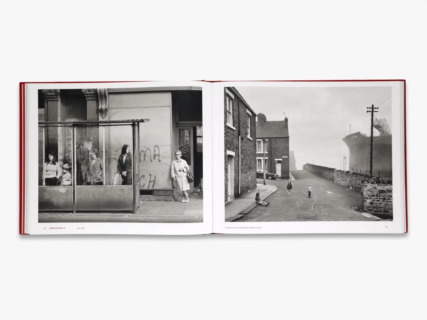 Photograph of an open book laid on a white surface, its pages featuring two large black-and-white images by Chris Killip of Britain in the 1970s; on the left, women and children wait at a bus stop and on the right, three children are in a street between some brick houses and, at right, a giant ship