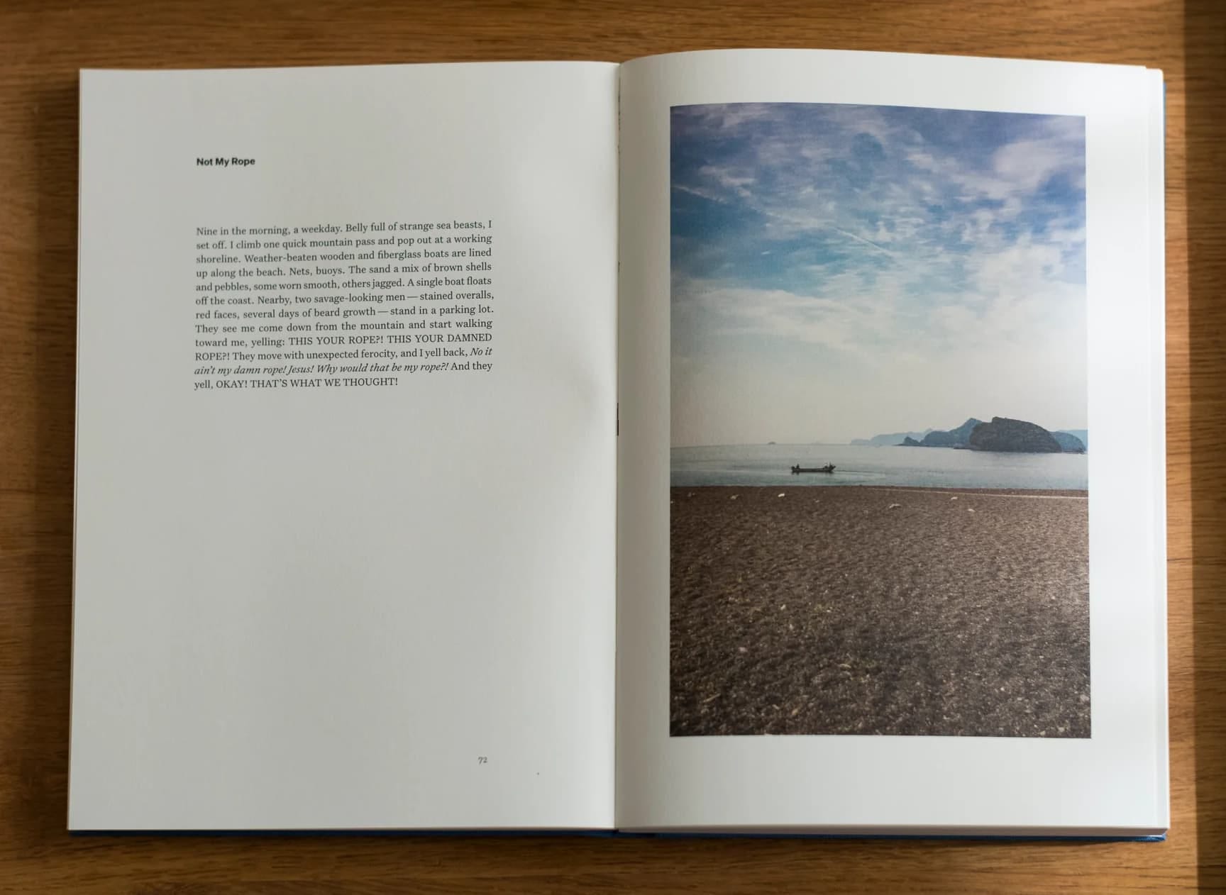 Photograph of an open book on a wood table; there is text on the left-hand page and a landscape photograph on the right-hand page